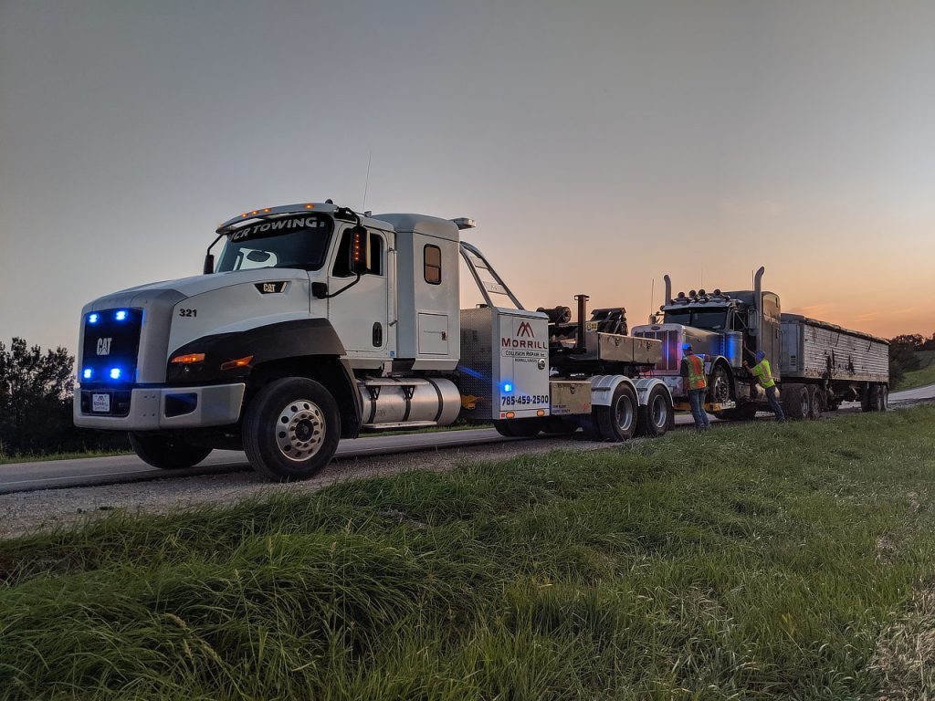 MCR Towing heavy wrecker towing a blue semi and trailer on a rural highway at dusk