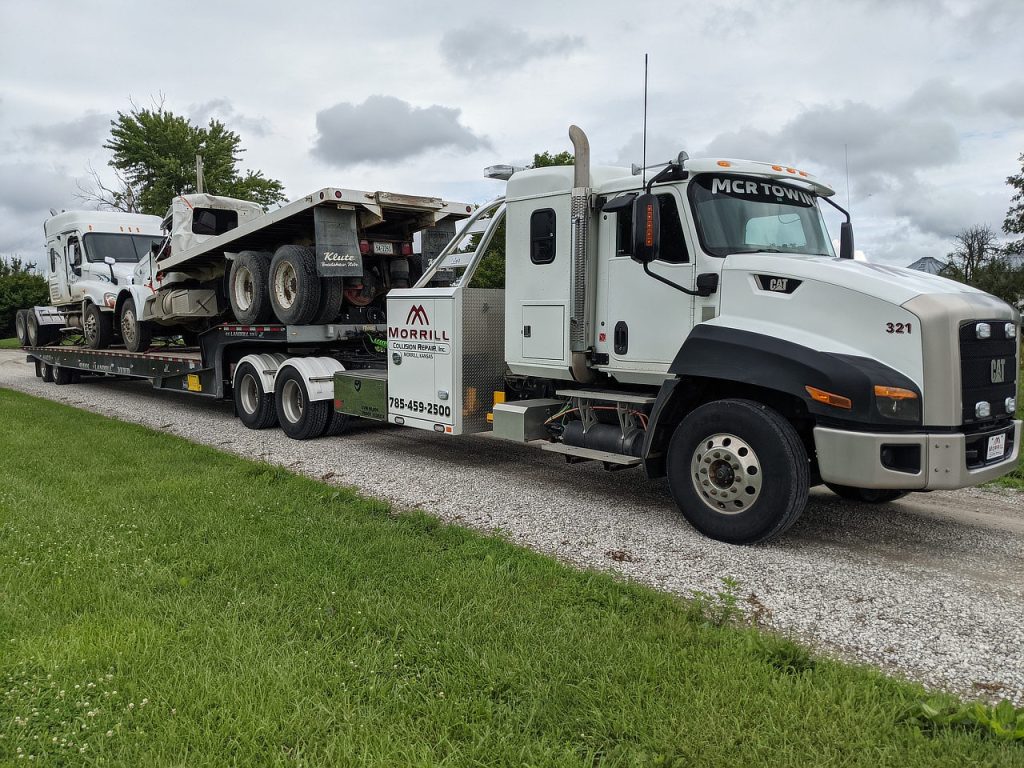 MCR Towing Cat CT660 pulling a drop-deck trailer loaded with two damaged white semi trucks