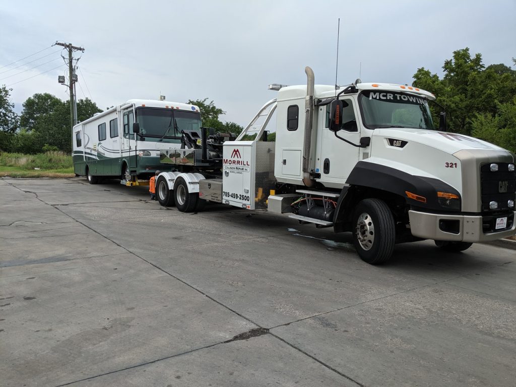 MCR Towing Cat CT660 heavy wrecker towing a green-and-white motorhome across a concrete lot