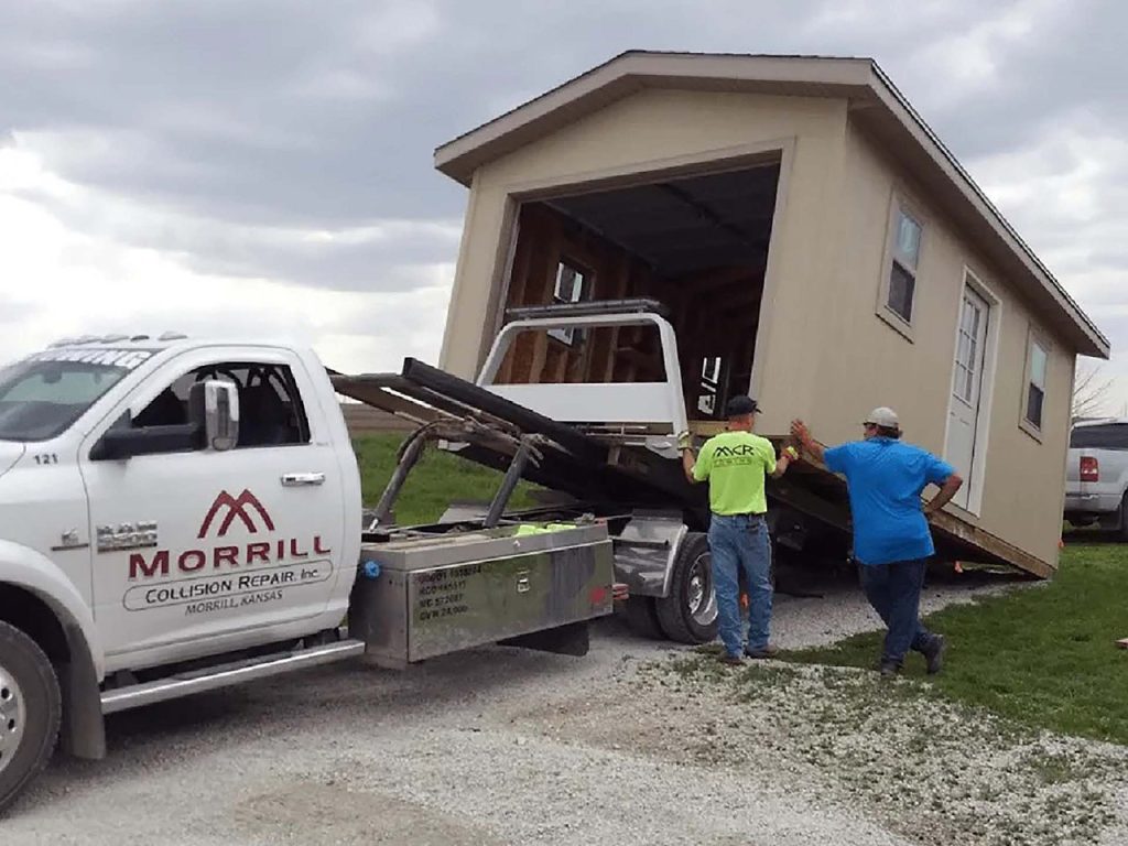 MCR Towing rollback truck loading a portable storage shed while two men guide it on