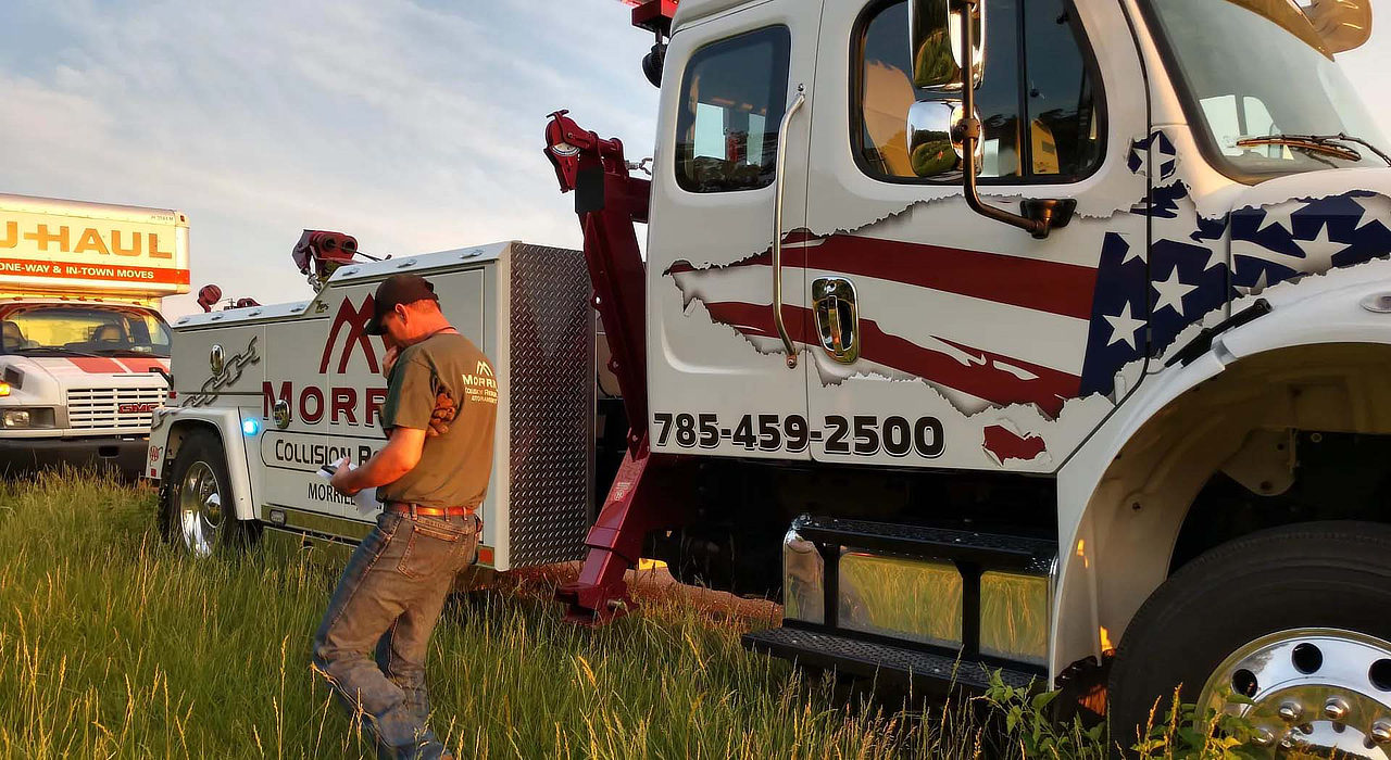 MCR Towing operator beside his wrecker at the roadside, a U-Haul truck in tall grass