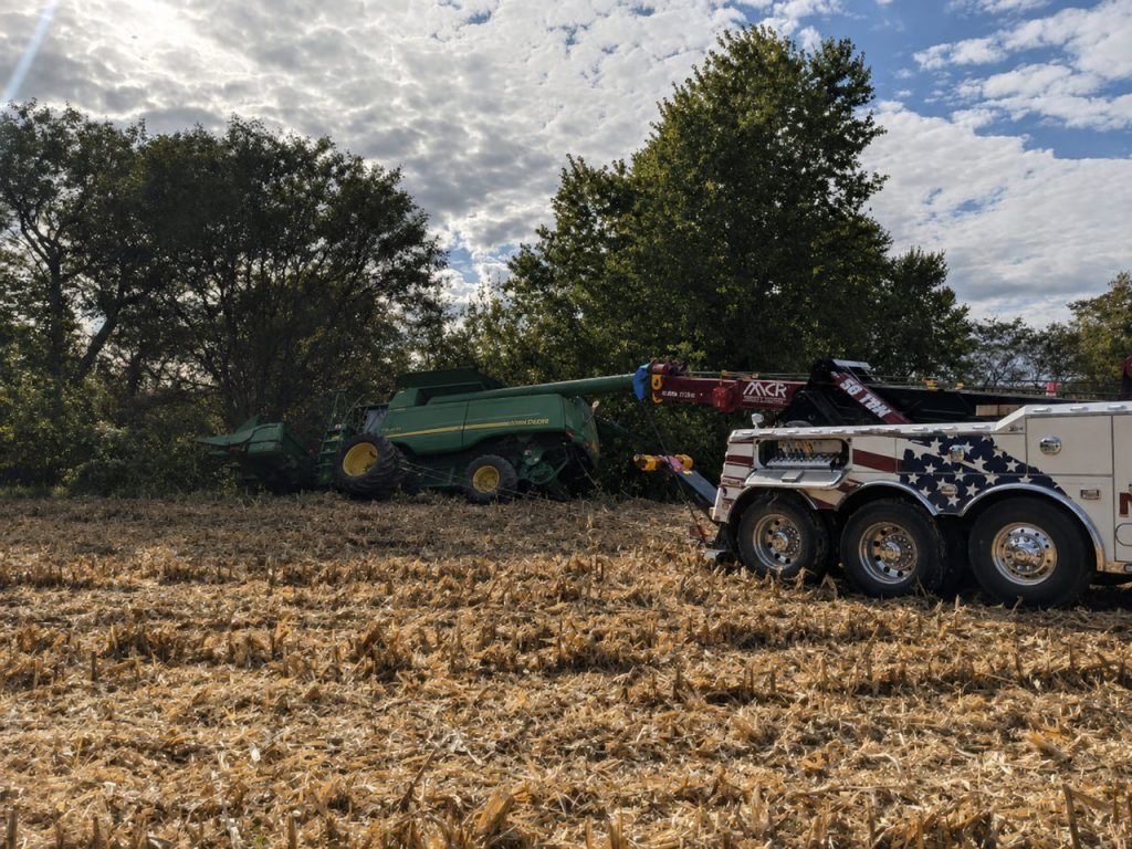 MCR Towing heavy wrecker rigged to a John Deere combine stuck in a tree line