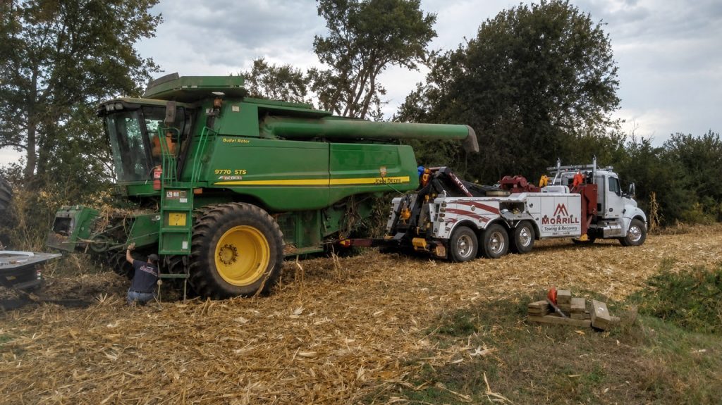 MCR Towing heavy wrecker hooked to a John Deere 9770 combine in a harvested field