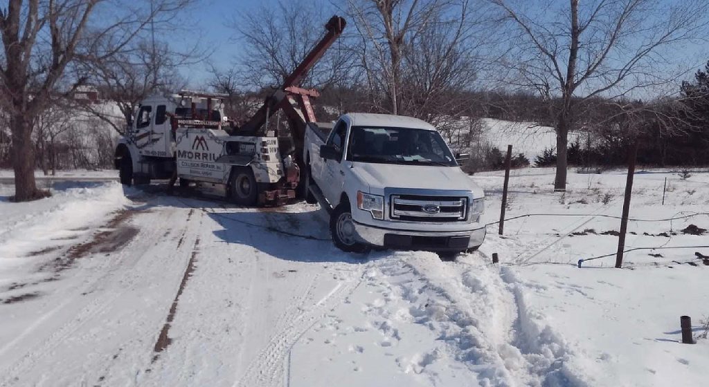 MCR Towing wrecker pulling a white Ford pickup out of a snowy ditch