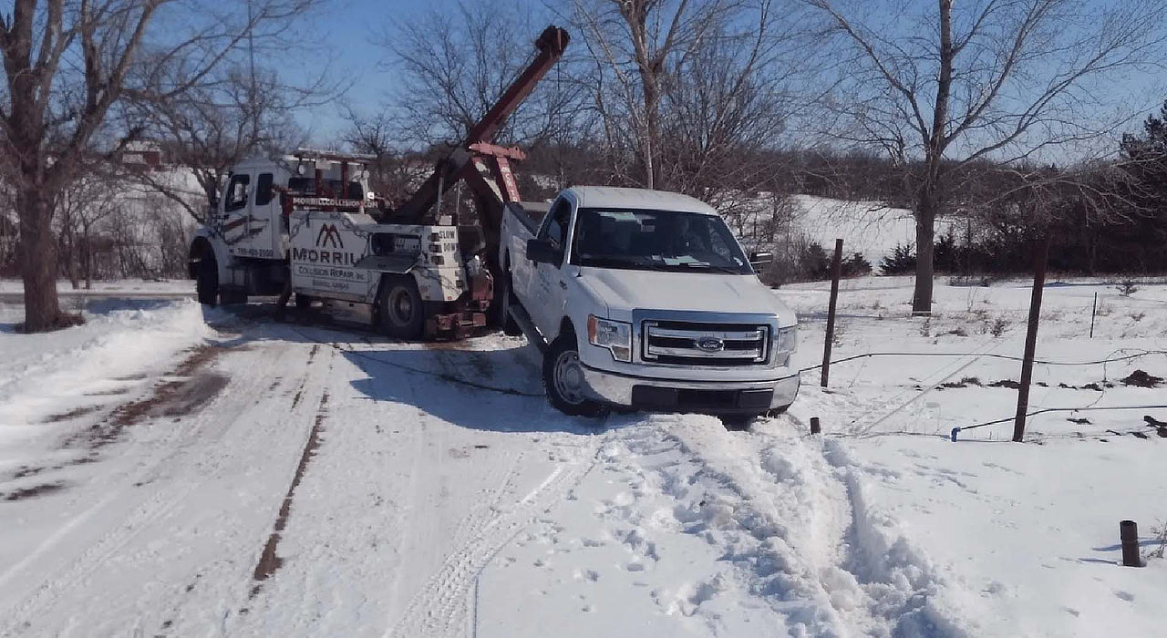 MCR Towing wrecker pulling a white Ford pickup out of a snowy ditch