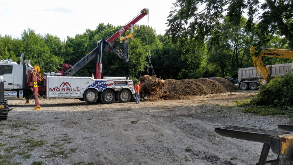 MCR Towing heavy wrecker lifting a large tree stump at a work site, excavator nearby